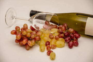 Red grapes, white grapes, bottle of wine and wine glass on neutral background