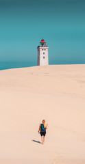 A travel girl exploring the giant empty sand dunes with the famous light house Rubjerg Knude in the danish landscape. Denmark, Europe