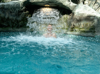 young sexy blond woman enjoys the falling water behind the waterfall in the spa pool