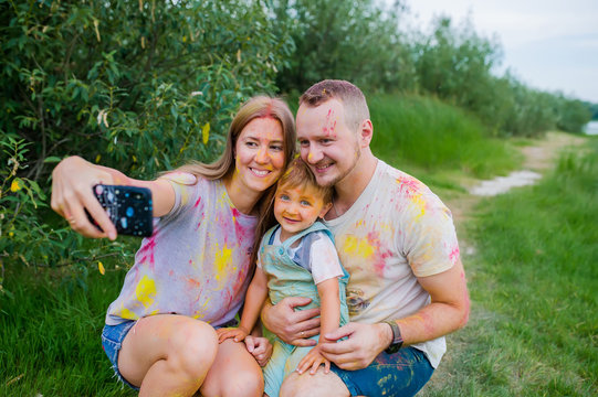 Smiling family in multi-colored paints taking selfie on summer meadow. Family portrait