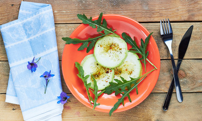 Zucchini cooked with spices and cheese and arugula vegetable salad in a living coral plate served with flowers on wooden rustic table, flat lay, overhead top view, closeup, copy space