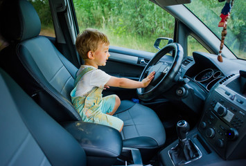 Funny boy with dirty face stained with paint holding hands on steering wheel in the car.