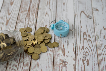 jar of coins with analog alarm clock on vintage wooden table.Financial and investment concept.