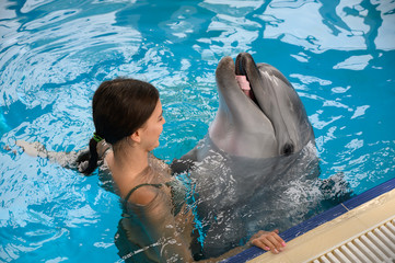 Obraz premium young beautiful brunette woman in a swimsuit swims and plays with a funny cute sea dolphin. Emotional rest in the water park. positive emotions, communication with marine mammals