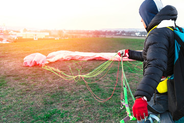 Man folds parachute after landing on green field