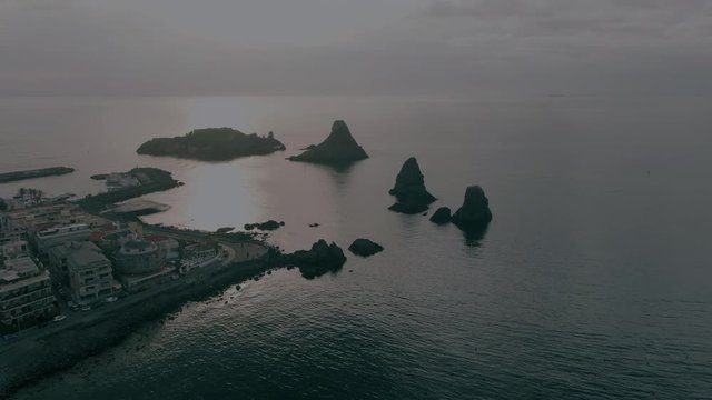 Aerial orbiting view of the fishing village of Acitrezza in East Sicily and the Faraglioni, basalt formations in the sea