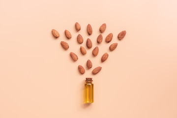 Creative layout. Flat lay natural almond oil in a bottle and almonds on a pastel pink background....