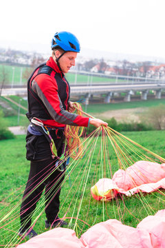 Landed young male paraglider raises parachute from ground
