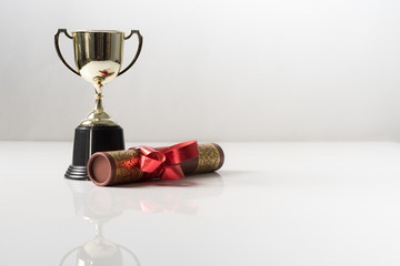 Golden trophy and graduation scroll on white table.Education concept.