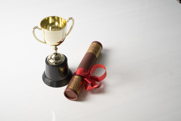 Golden trophy and graduation scroll on white table.Education concept.