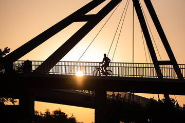 Düsseldorf 2019: Silhouette of a male person riding a bike on bridge over the rhine in sunset