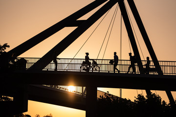 Düsseldorf 2019: Silhouette of several Pedestrians and a female person riding a bike on the bridge over the rhine in sunset