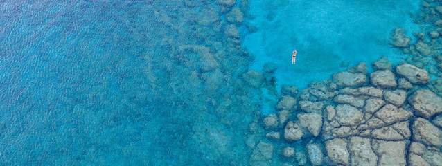 An aerial view of the beautiful Mediterranean Sea, with a lonely swimmer, where you can see the rocky textured underwater corals and the clean turquoise water of Protaras, Cyprus