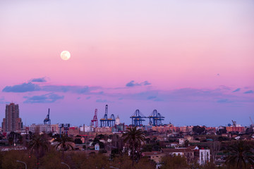 Industrial city,  cranes and container port terminal at night with big moon in colourful sky