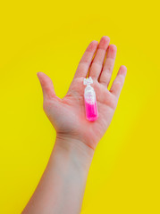 Female hand holding one pink liquid medicine in an ampoule, isolated on yellow background.