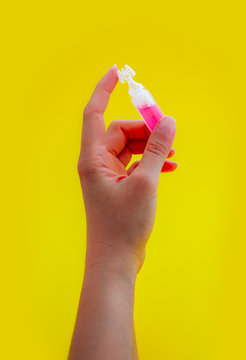 Female hand holding one pink liquid medicine in an ampoule, isolated on yellow background.