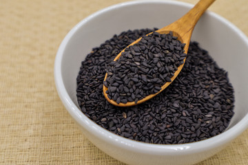 Black sesame seeds in white cups and wooden spoons on brown tablecloths are suitable for graphic or vocal work.