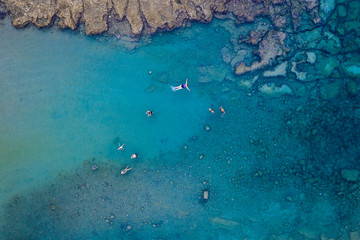 An aerial view of the beautiful Mediterranean sea, full of swimmers, where you can see the rocky textured underwater corals and the clean turquoise water of Protaras, Cyprus