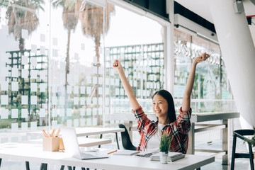 young studebt sitting at table in library college writing and working  and arms up celebrating, education concept
