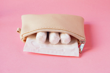 female intimate hygiene products - sanitary pad and tampons in white handbag on pink background