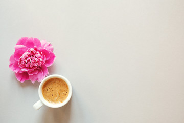 morning cup of coffee and fresh beautiful spring pink peony flower on light background, top view, flat layout, copy space