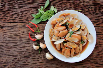 Stir fried clam with chili paste and thai basil leaf in white dish,On the wooden, This is thai food cuisine.