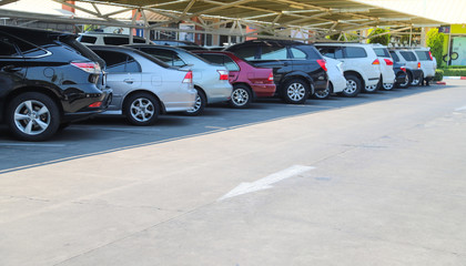 Closeup of rear, back side of black car with  other cars parking in parking lot under roof in bright sunny day.