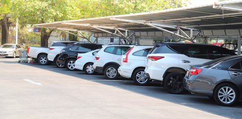 Closeup of rear, back side of white car with  other cars parking in parking lot under roof in bright sunny day. 