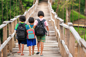 Asian primary school girls walking across suspension footbridge at dusk. - 277197967