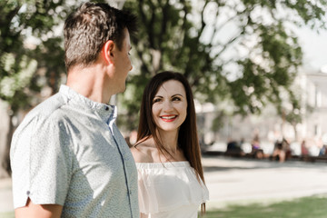 Naklejka premium Young couple on the street in summer. Man and woman in love having a walk outdoors. Beautiful pair hugging and looking at each other in European city. Dating concept. Love story