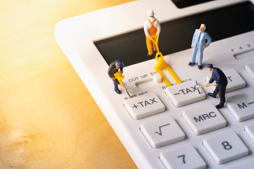 Miniature workers digging tax button on calculator