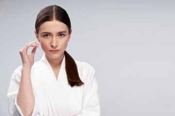 Attractive young woman in bathrobe standing against light blue background