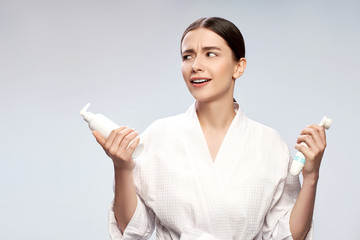 Cute girl in bathrobe holding bottle of cosmetic cream and pore cleansing brush
