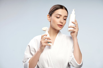 Attractive young lady holding bottle of cosmetic cream and pore cleansing brush