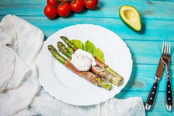Grilled green asparagus wrapped with bacon, benedict poached egg on blue wood background.