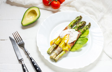 Grilled green asparagus wrapped with bacon, benedict poached egg on white wood background.
