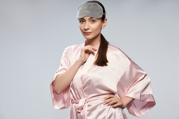 Beautiful young woman in pink silk robe standing against light blue background