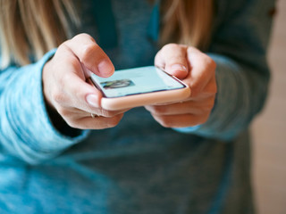 Close up of a woman's hands holding mobile smartphone and holding paper coffee cup at twilight outdoors rainy weather evening in trendy vintage film tones