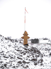 A lonely yellow fire hydrant with a red, orange and white flag stands on top of a mound of snow...