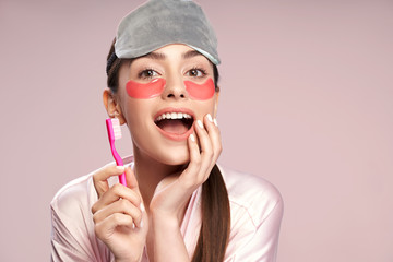 Charming girl with under-eyes patches holding toothbrush and touching her face