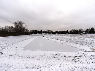 A frozen man made retention pond covered in ice and fresh white snow awaiting surrounding construction development in rural Wisconsin in the winter season.