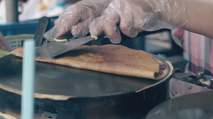 skilled chef in gloves folds delicious fried pancake with filling on hot crepe maker with spatula in cafe closeup