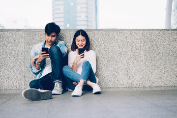 Asian couples of happy smiling sitting using smartphone in covered walkway.The concept of using the phone is essential in everyday life.