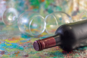 A bottle of cold red wine and two glasses on a colored background with bokeh effect