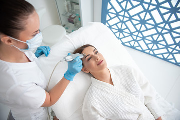 Fototapeta premium Smiling young lady on suprasonic beauty procedure