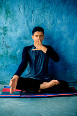 Portrait shot of the young man doing pranayama or pranayam or breath control yoga on a colorful mat...