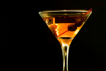 A martini glass with green olives on a black background