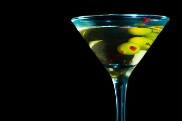A martini glass with green olives on a black background