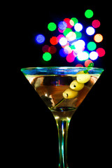 A martini glass with green olives on a black background