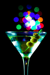 A martini glass with green olives on a black background